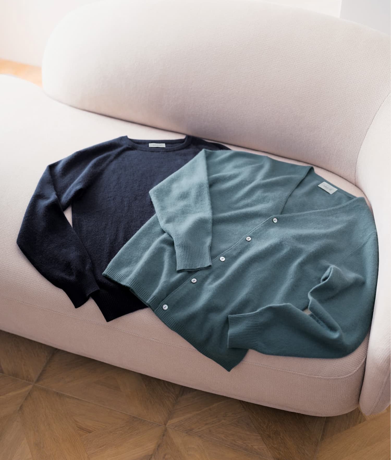 白いソファの上に2つネイビーとスモーキーブルーのセーターが置かれた写真