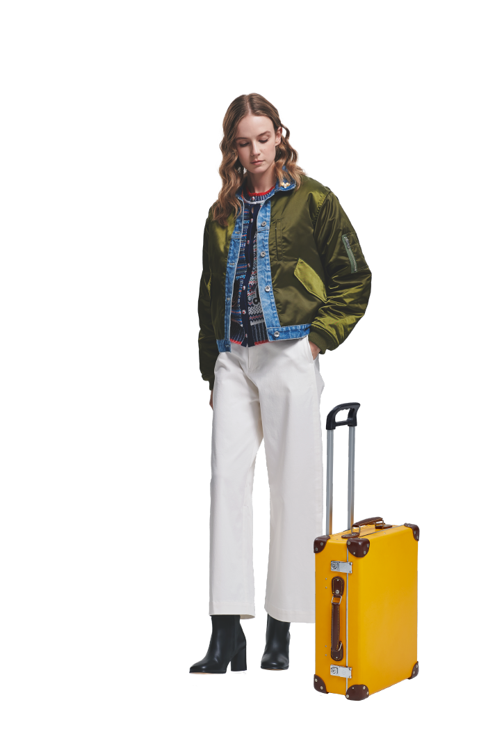 カーキ色のコートを着た黄色のトランクを近くに置く女性の写真