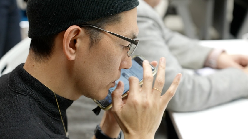 画像：ブラインド・コミュニケーターがスマートフォンでWEBサイトの読み上げ機能を検証している様子　画像おわり