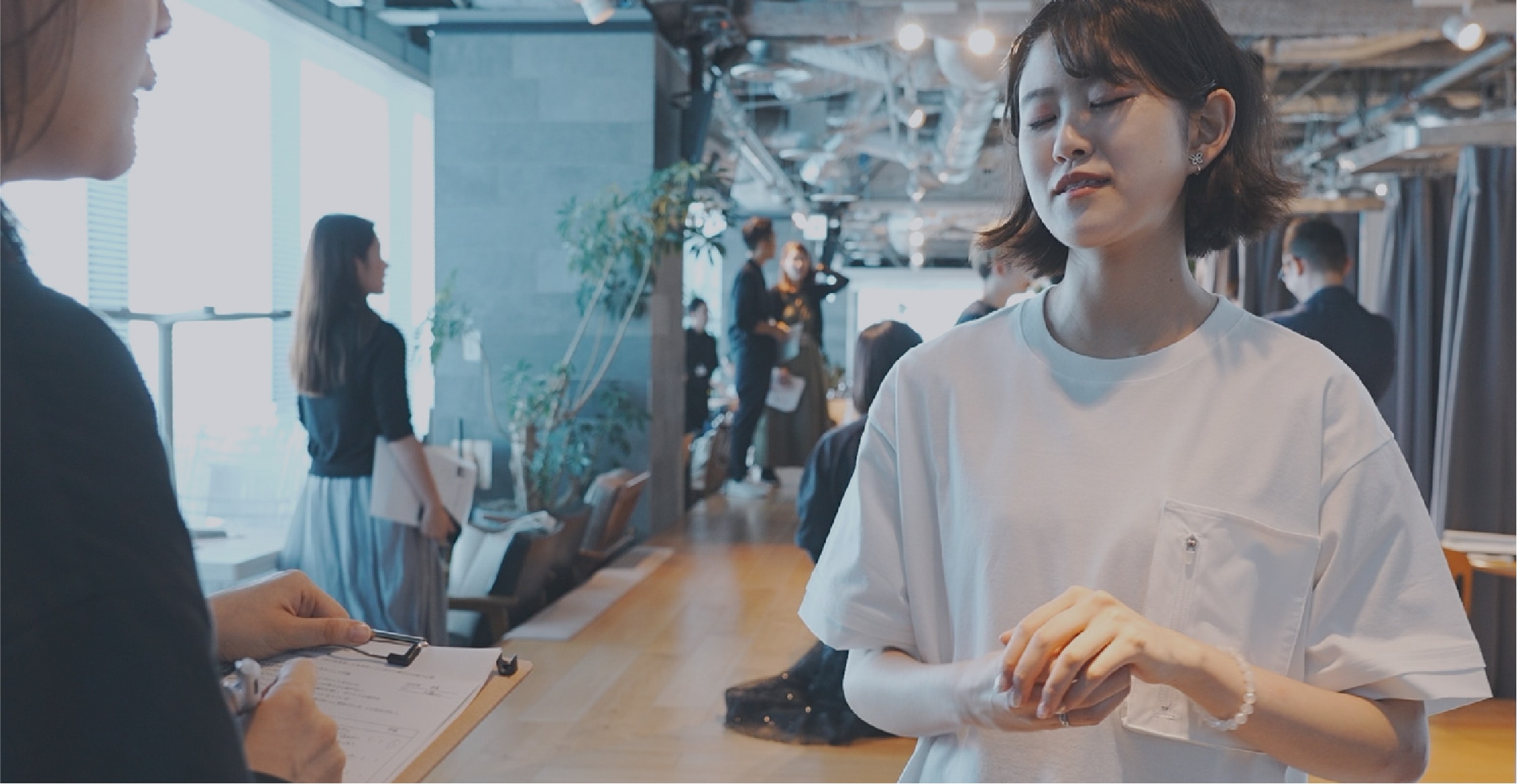 画像:ワークショップの様子。視覚障がい者の女性が、白いカットソーを試着している。 画像おわり