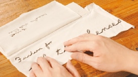 画像:テーブルに置かれた刺繍のサンプルを、視覚障がい者が両手で触れて確かめている様子。 画像おわり