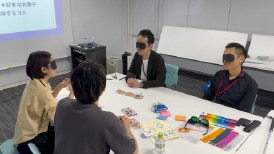 画像:アイマスクを着けたバイヤー3名と視覚障がい者の男性が対話をしている様子。 画像おわり
