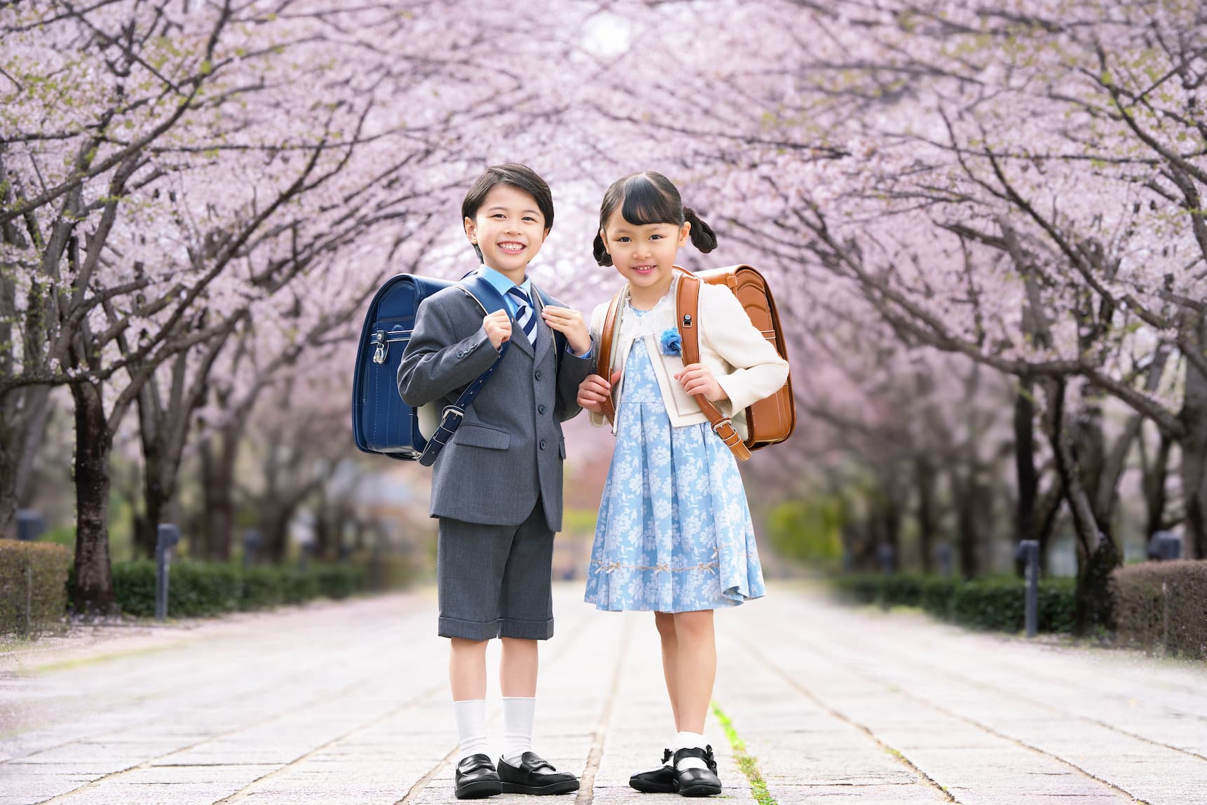 桜を背景にランドセルを背負った男の子と女の子が並んでいる写真