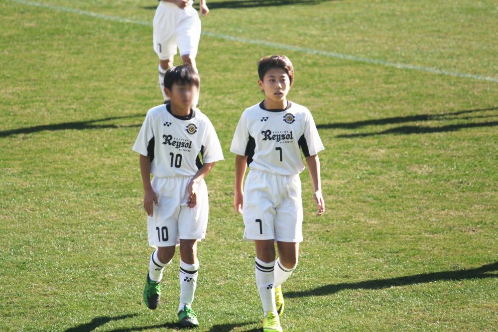 右が小学生時代の細谷真大さん 柏レイソルアカデミーの白いユニフォーム姿でチームメイトと並んで芝生のグラウンドを歩いている様子 現在の面影を残しながらもあどけなさの感じられる少年時代の写真＜alt＞
