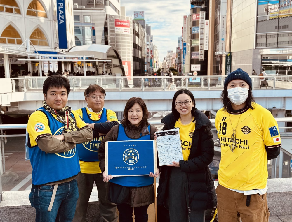 柏駅前でフリーペーパーや看板を持つ柏でよりみち アディショナルタイムズの配布メンバー5人
