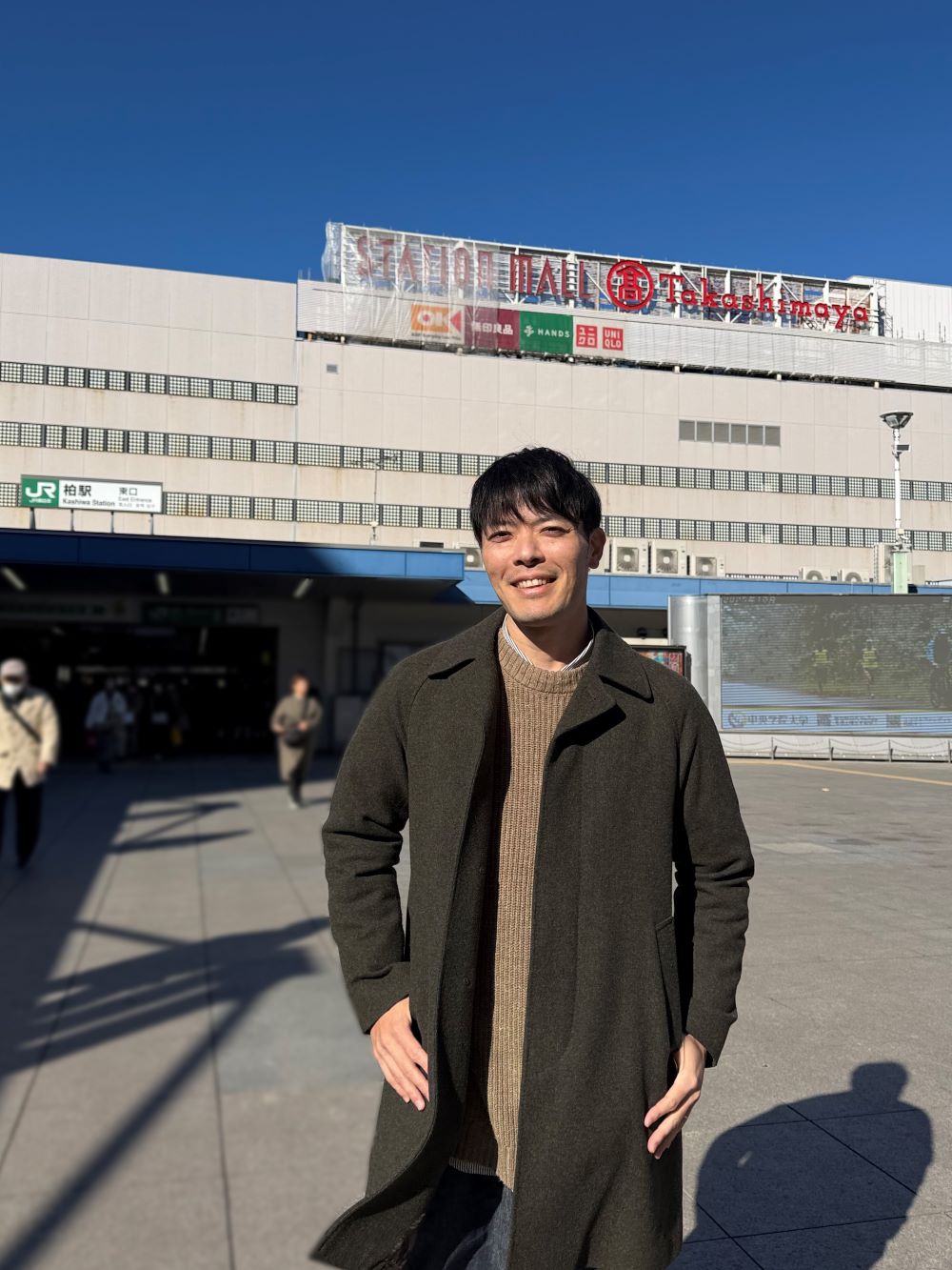 柏駅のダブルデッキで柏高島屋を背にしてポーズをつけながら微笑む藤田さん