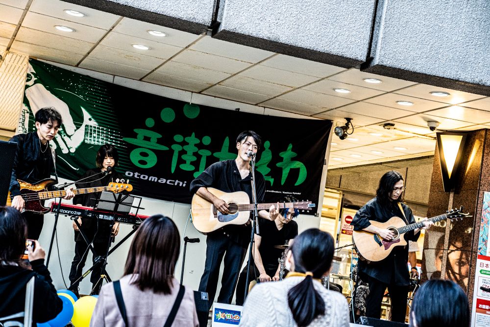 柏の音楽イベント音街かしわのにて柏高島屋本館エントランスステージでバンドメンバーと一緒にライブをする藤田さんの様子