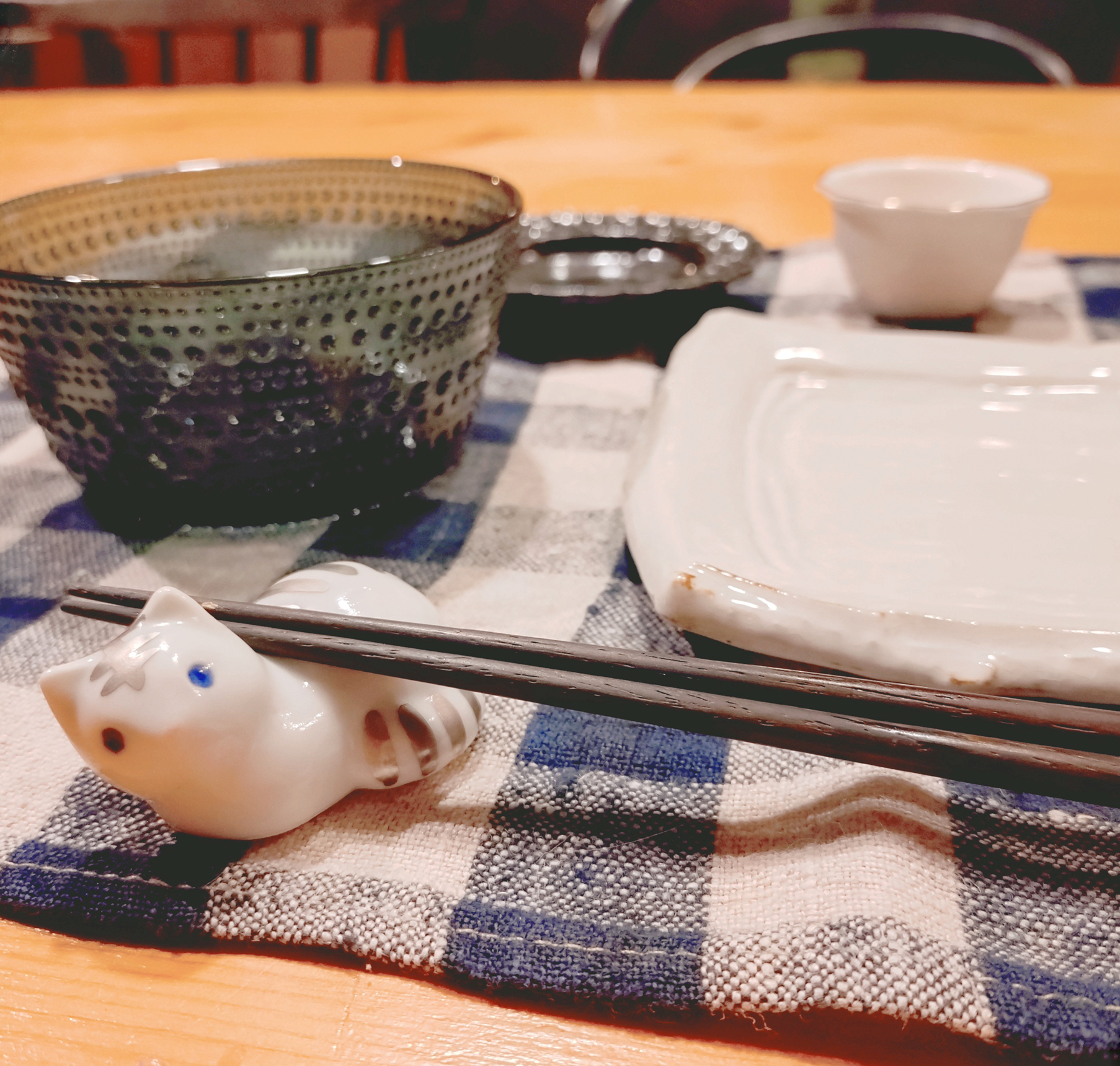 Tさんの自宅の食卓にお皿やガラスボウルが並べられ、プラチナ彩の猫の箸置きがこちらを愛らしい表情で見つめているかのように見える様子