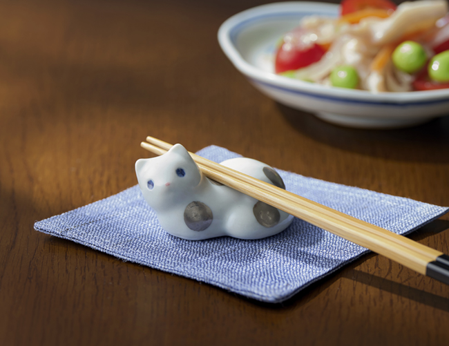 奥に料理が盛られた小皿が並び、手前にはこちらを見つめるプラチナ彩の猫の箸置きに箸が置かれている様子