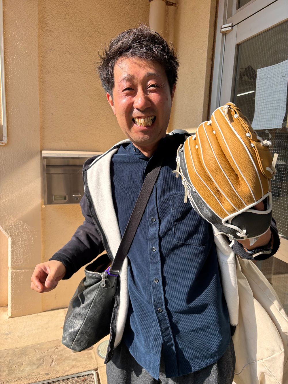 野球のグローブを左手にはめ、満面の笑みを浮かべる柏レザー株式会社代表の飯島さん