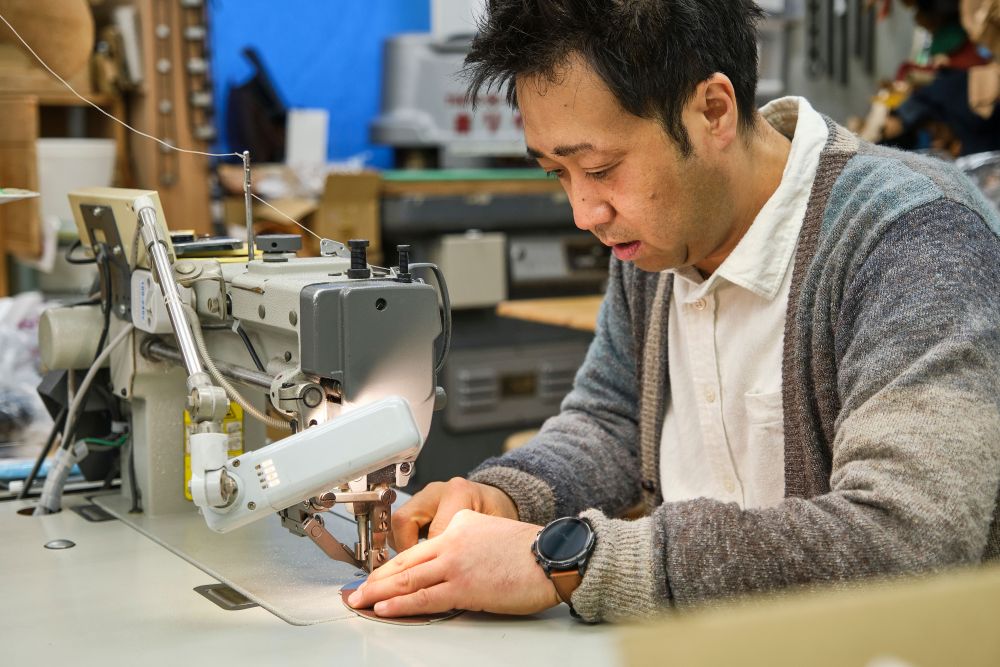 作業台に向かいミシンを動かす柏レザー株式会社代表の飯島さん