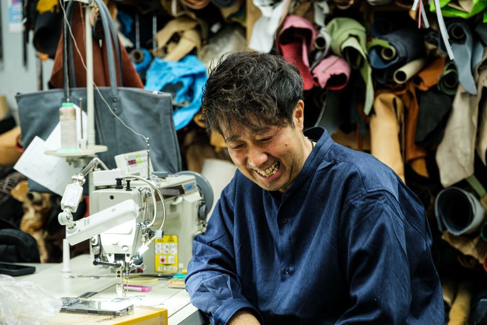 自身のカバン屋Haritoの作業場で、はにかみ笑いをする柏レザー株式会社代表の飯島さん