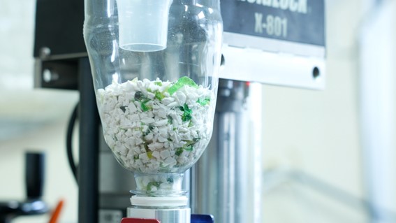 空容器を裁断してできたプラスチックのチップと白い再生プラスチックが工場の機械に入っている様子