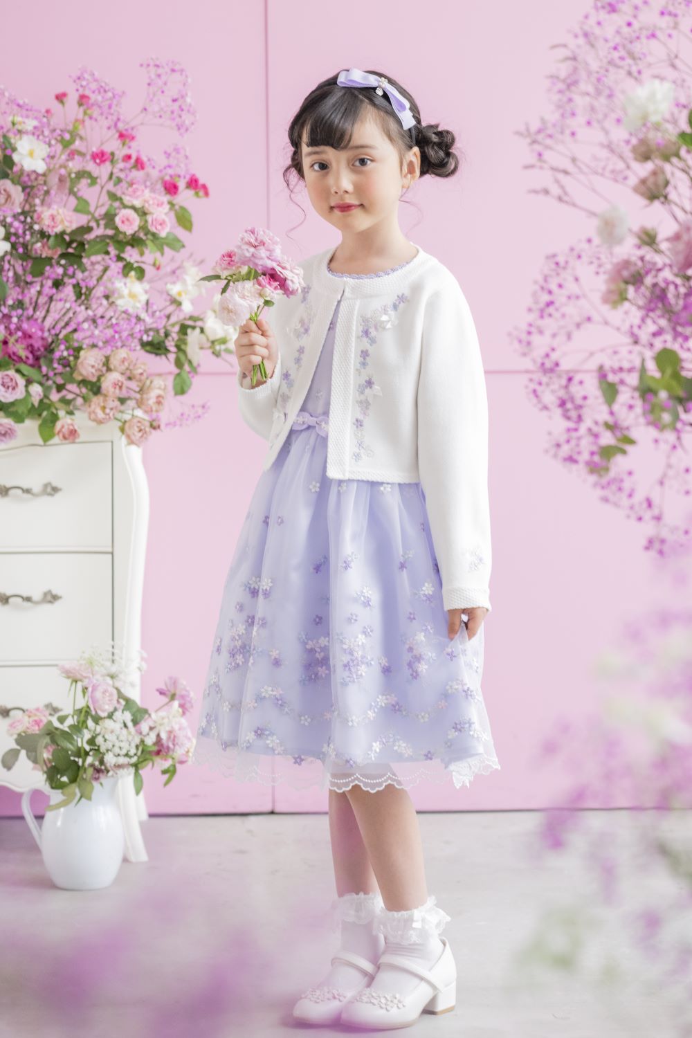 お花の刺しゅうが入ったワンピースとホワイトのニットカーディガンを着用した女の子