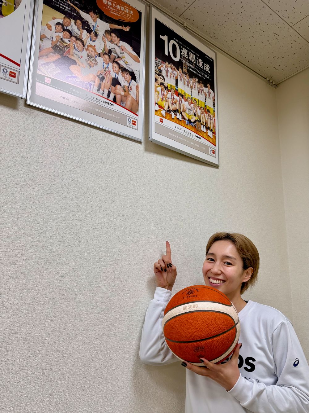 バスケットボールを持ちながら第19回バスケットボール女子日本リーグ優勝のポスターを指差し、嬉しそうに笑うENEOSサンフラワーズ宮崎早織選手